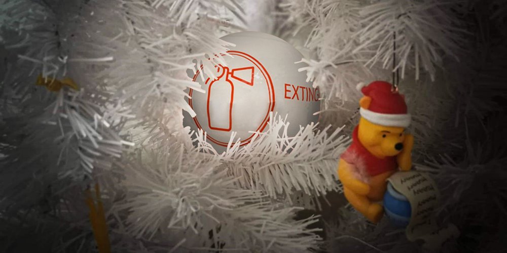 a white ornament marked "extinguisher ornament nestled in the boughs of a white artificial christmas tree