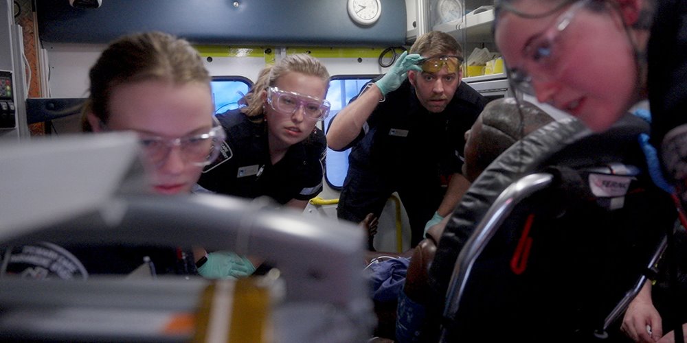 four student paramedics examine a patient in an ambulance